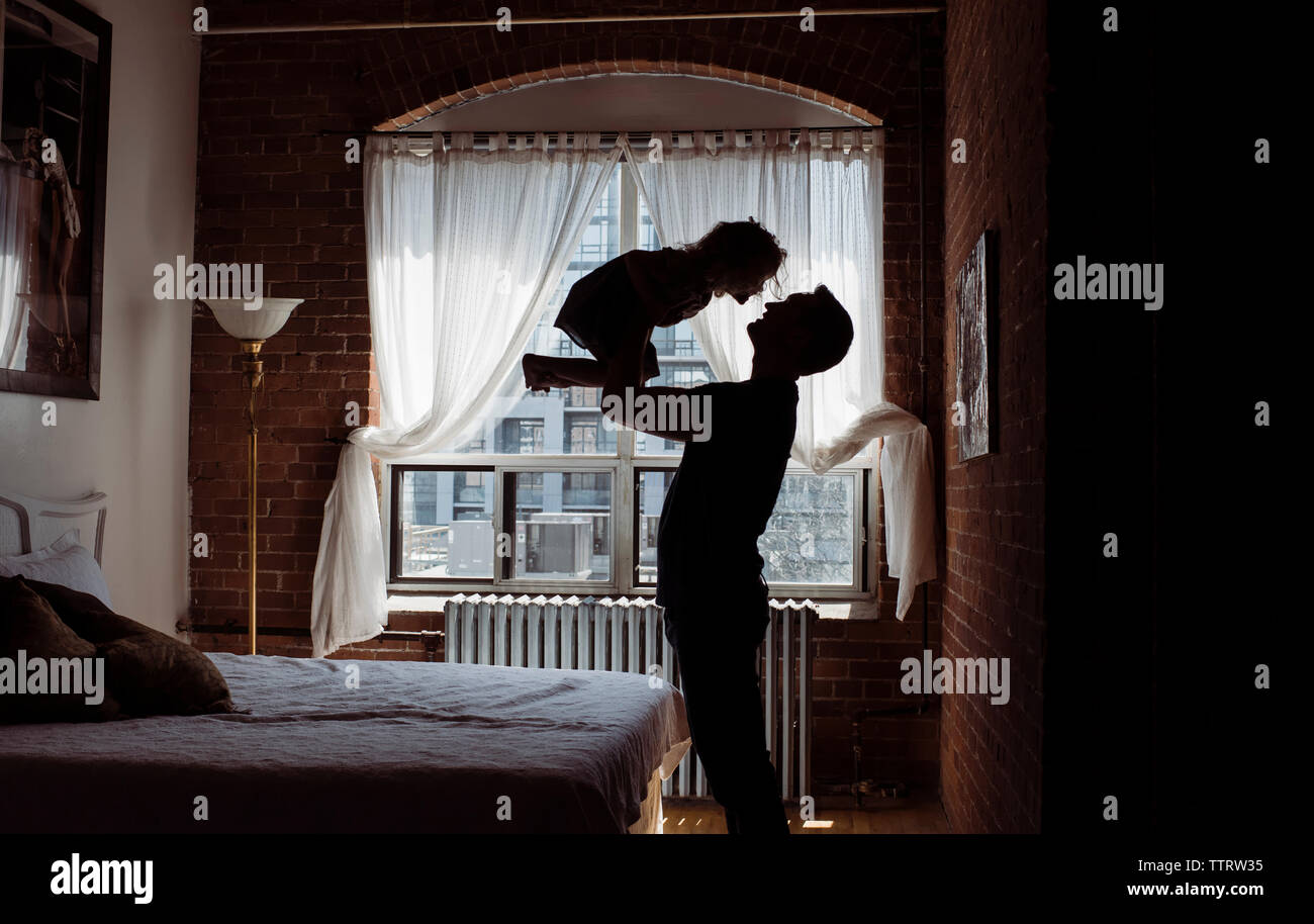 Silhouette father picking up daughter while standing by bed at home Stock Photo