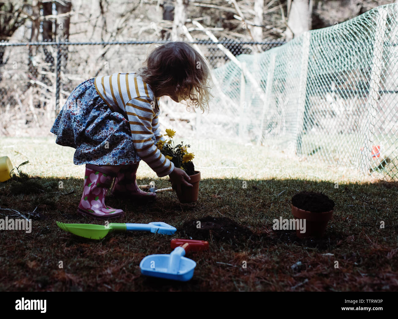 Side view of girl holding potted plant while standing on field in yard ...