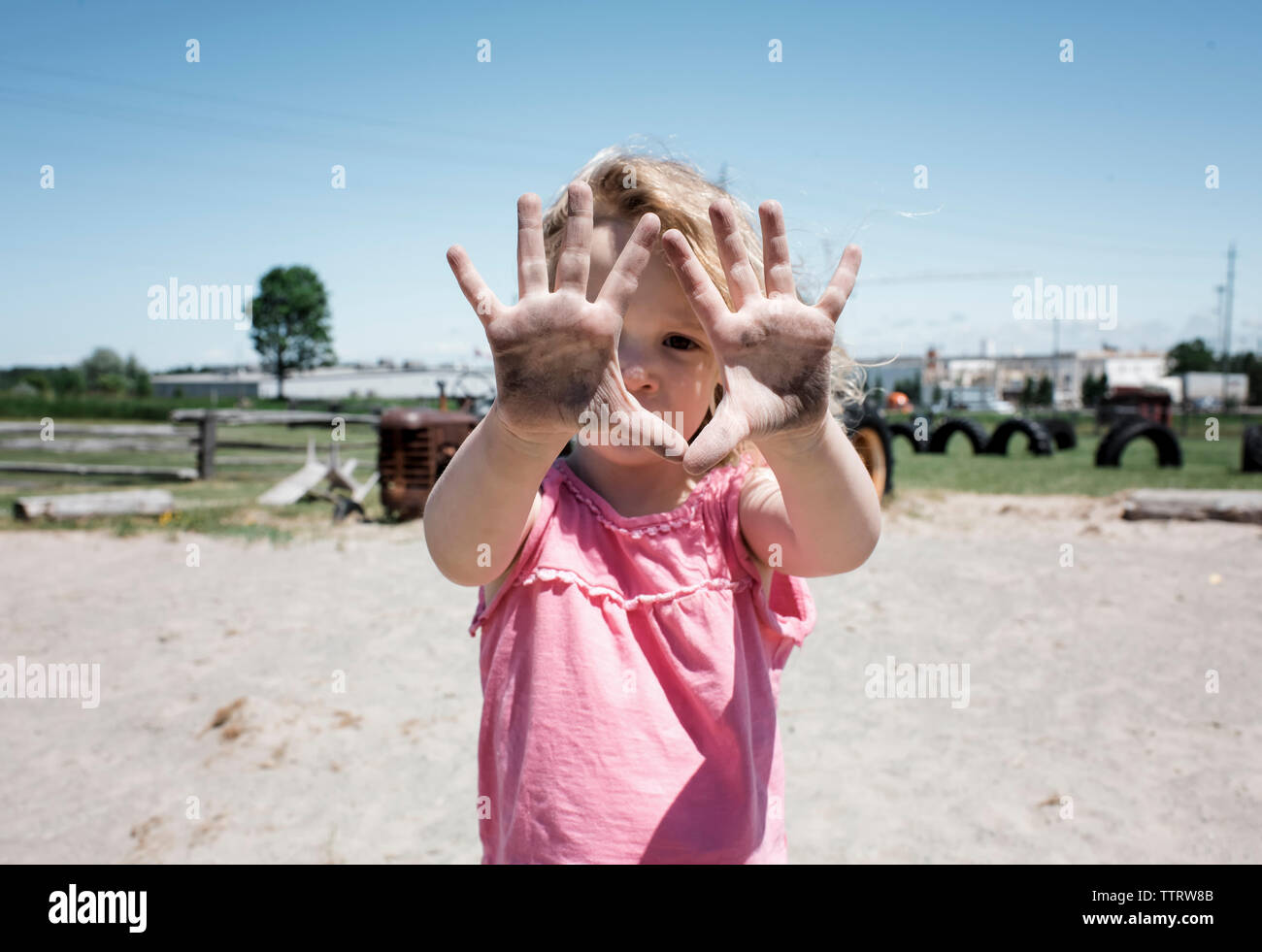 Portrait of girl showing dirty hands while standing on sand against clear sky at playground Stock Photo