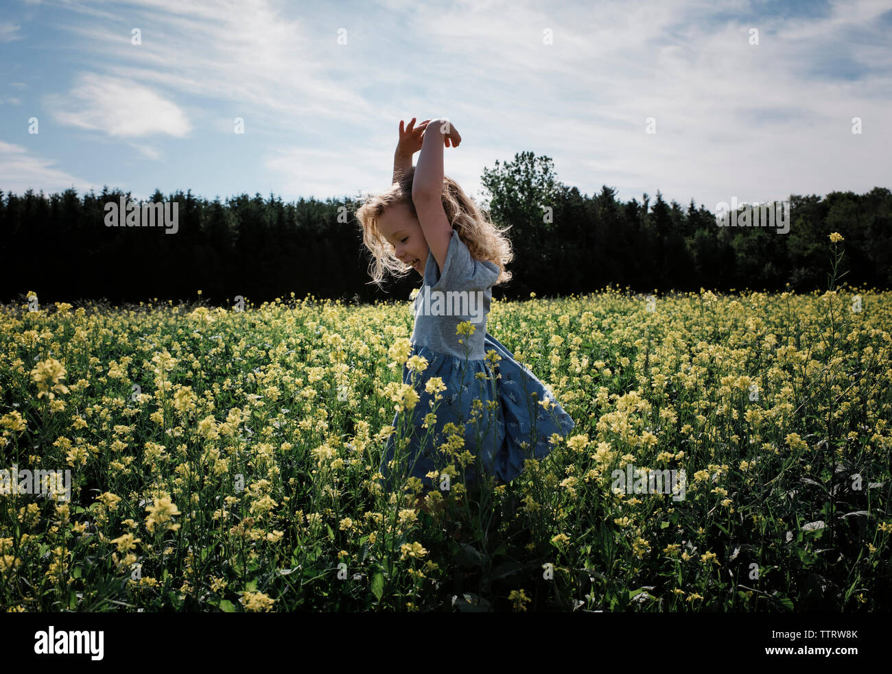 Happy girl with arms raised standing amidst plants against sky Stock Photo