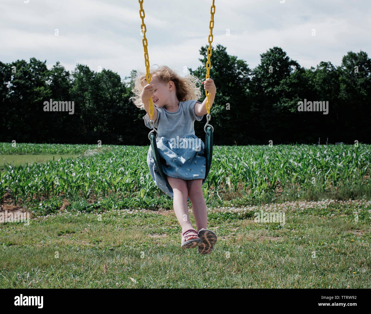 Happy girl swinging against sky at park during sunny day Stock Photo