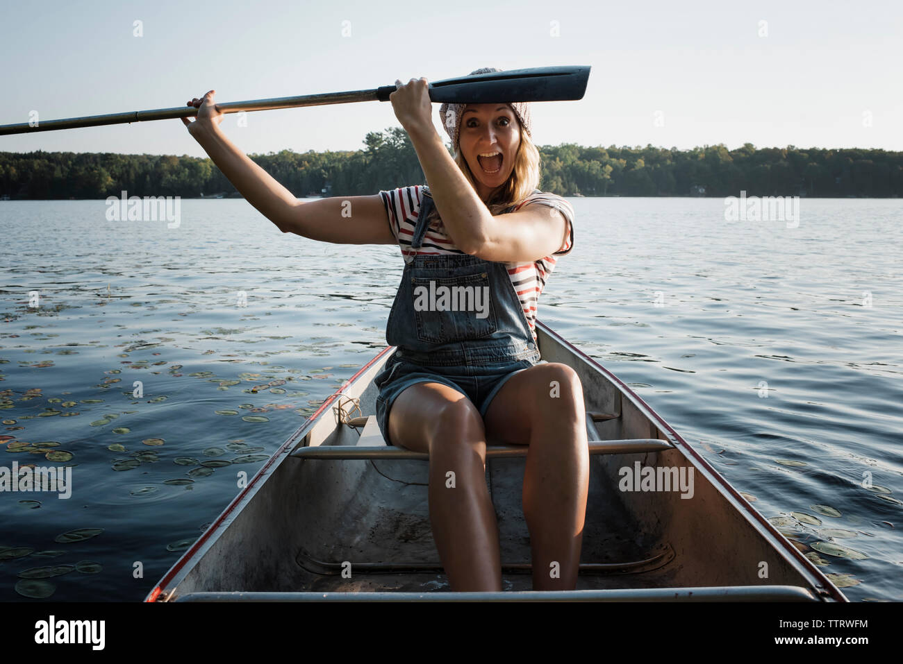 Portrait of happy woman with mouth open holding oar while sitting in boat on river against sky Stock Photo