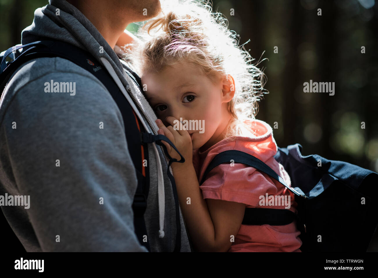 Midsection of father carrying cute daughter sucking thumb while standing in forest Stock Photo
