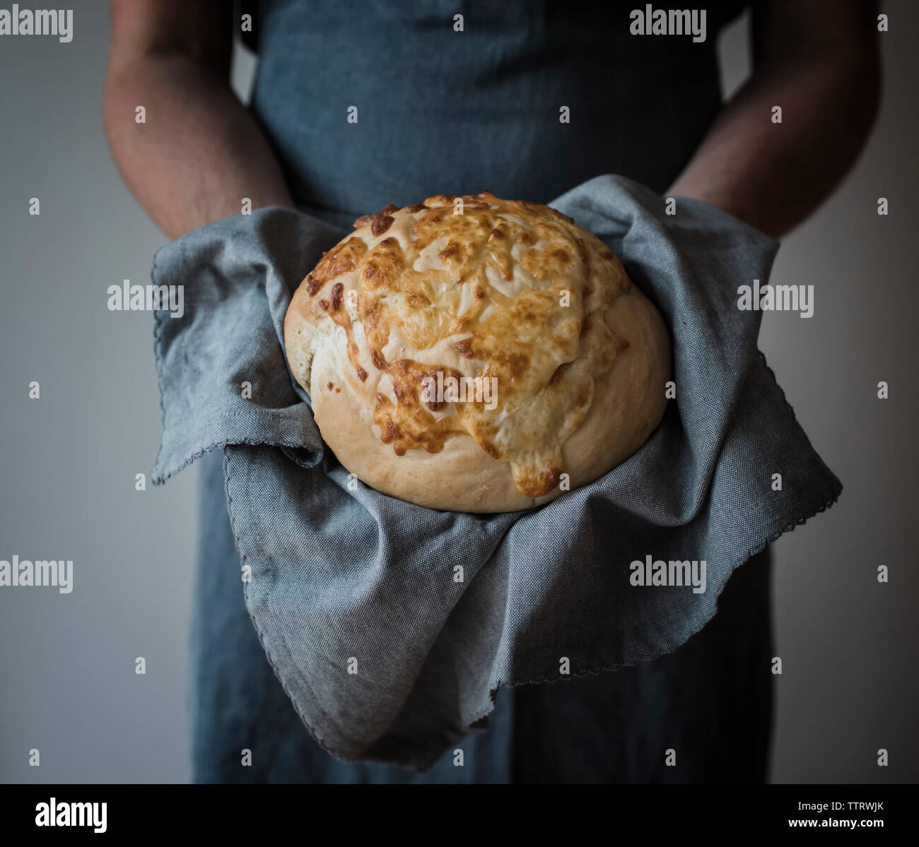 Midsection of woman holding bread with napkin while standing against wall at home Stock Photo