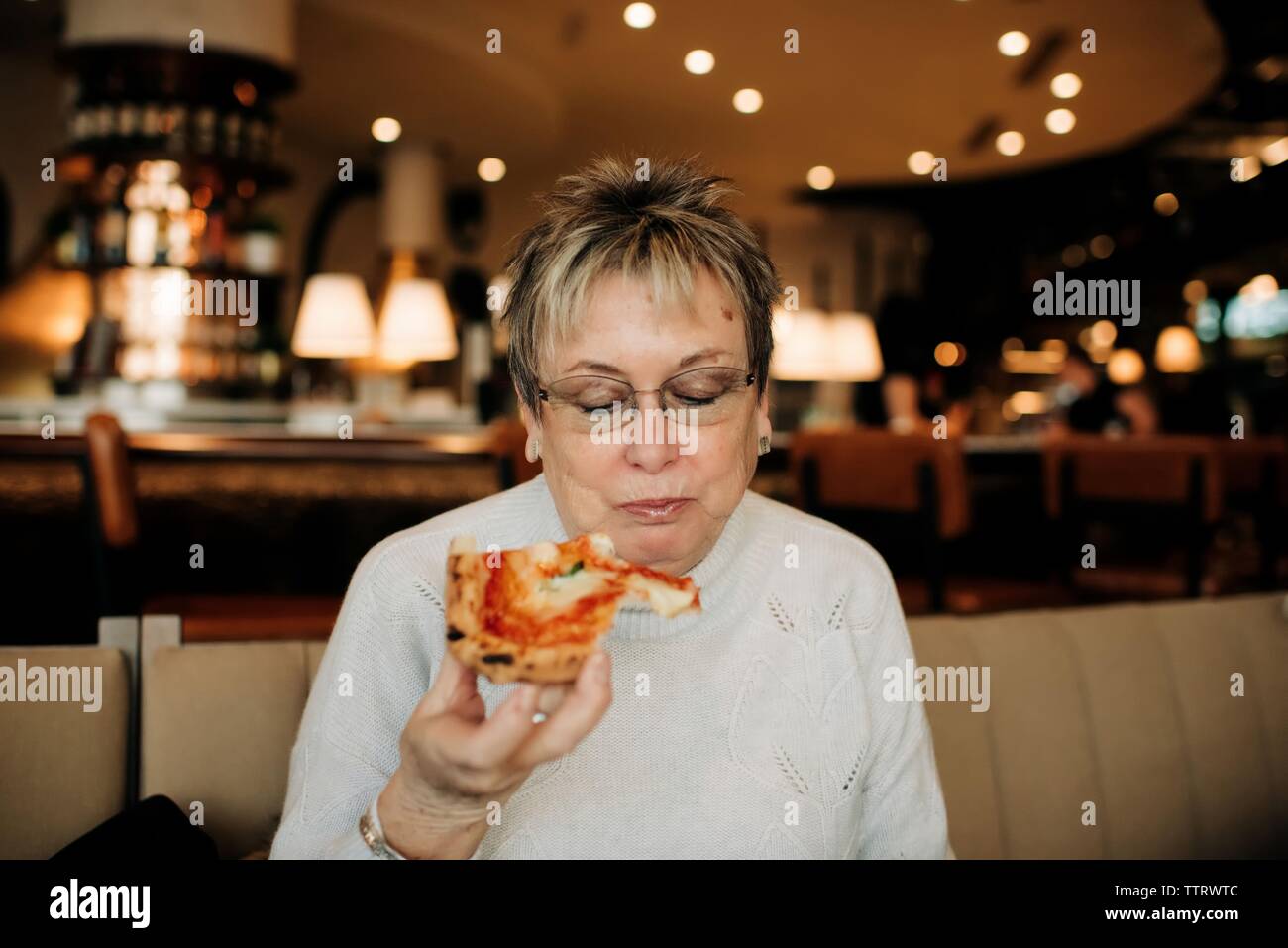 older lady holding pizza eating at a restaurant looking down reading Stock Photo