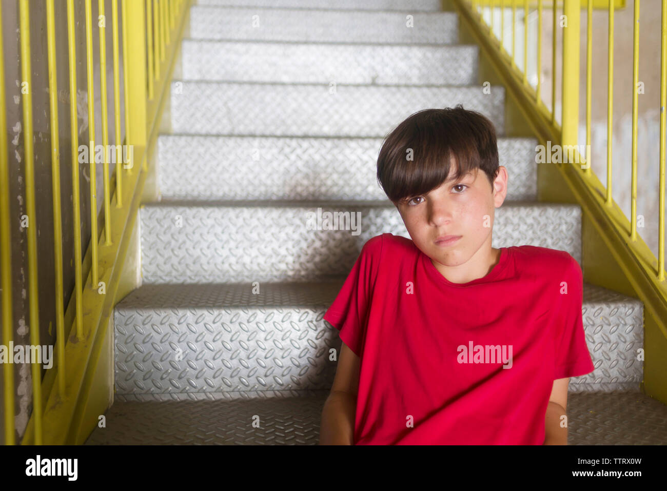 Portrait of confident student wearing red t-shirt sitting on metallic steps Stock Photo