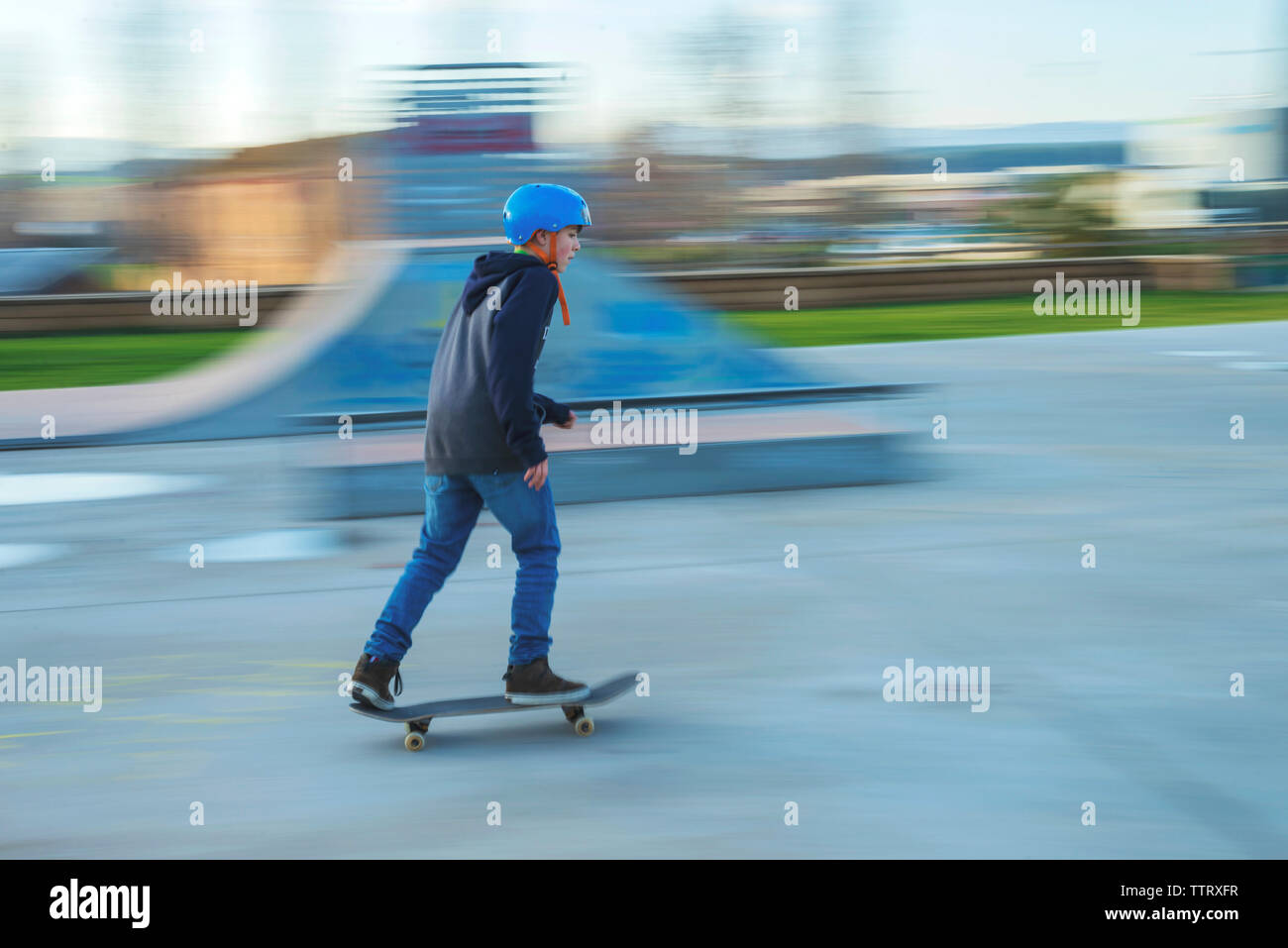 Side view of young skater wearing blue helmet in motion at skatepark