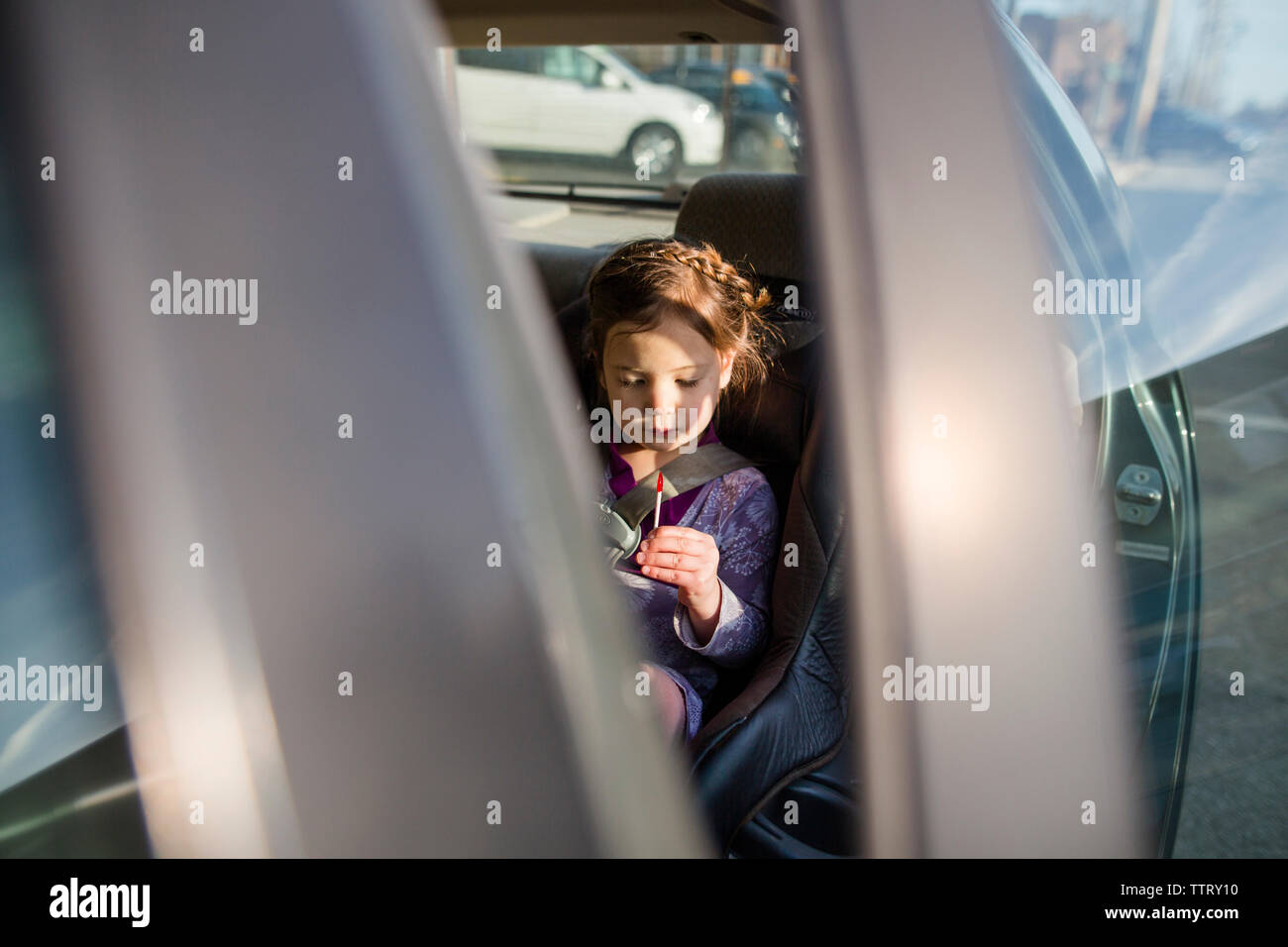 Girl looking at lollipop while sitting in car seen through vehicle door Stock Photo