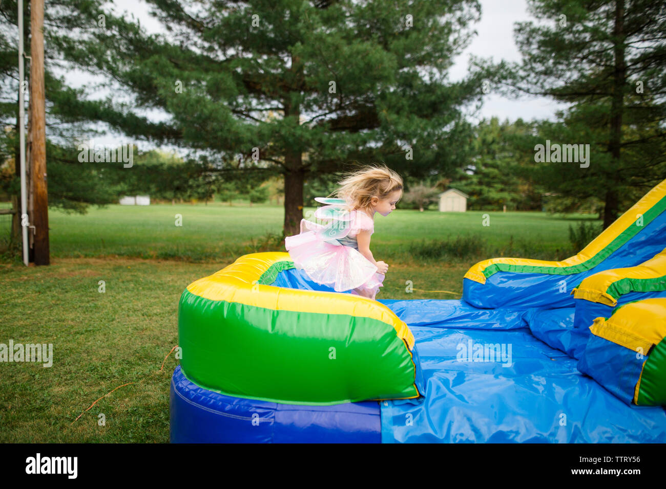 Girl in fairy costume jumping on bouncy castle at park during Halloween Stock Photo