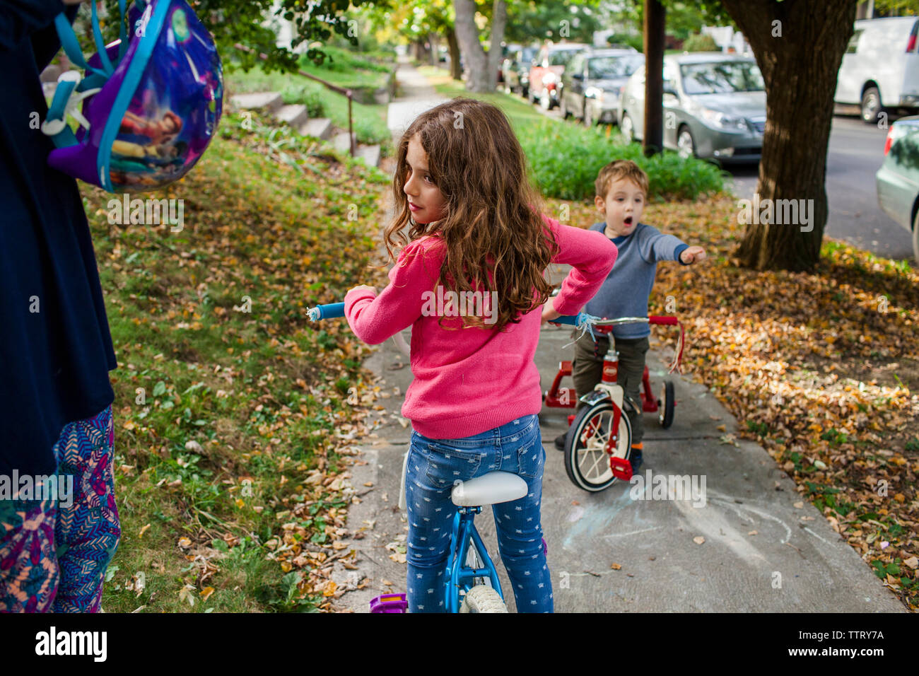 Midsection of mother holding helmet while children riding bicycles on footpath during autumn Stock Photo