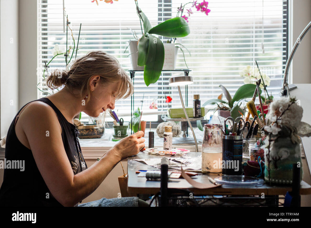 Side view of female sculptor sculpting at desk by window in workshop Stock Photo