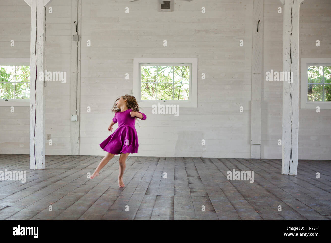 Happy girl dancing on hardwood floor against wall in barn Stock Photo