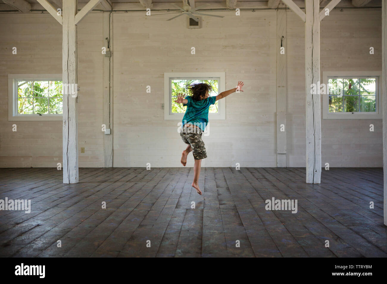 Rear view of happy boy dancing on hardwood floor against wall in barn Stock Photo