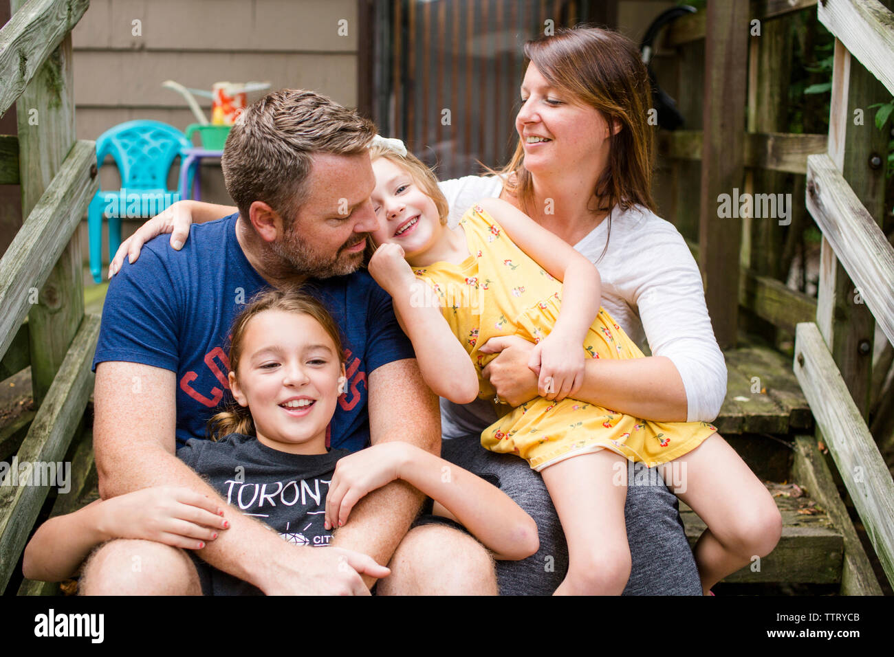 Happy family talking while sitting on steps against house in yard Stock Photo