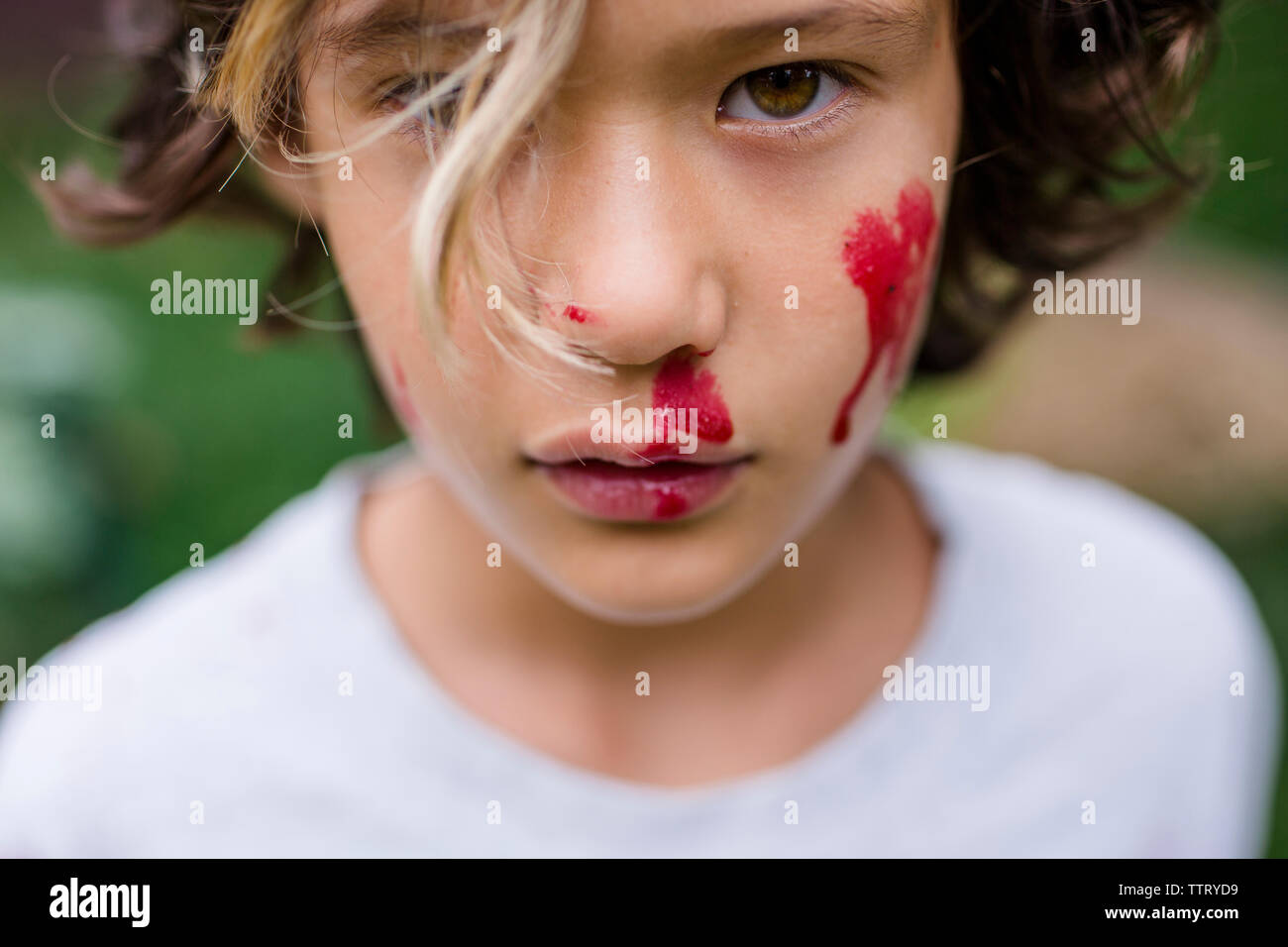 Close-up portrait of cute boy with red face paint standing in park Stock Photo