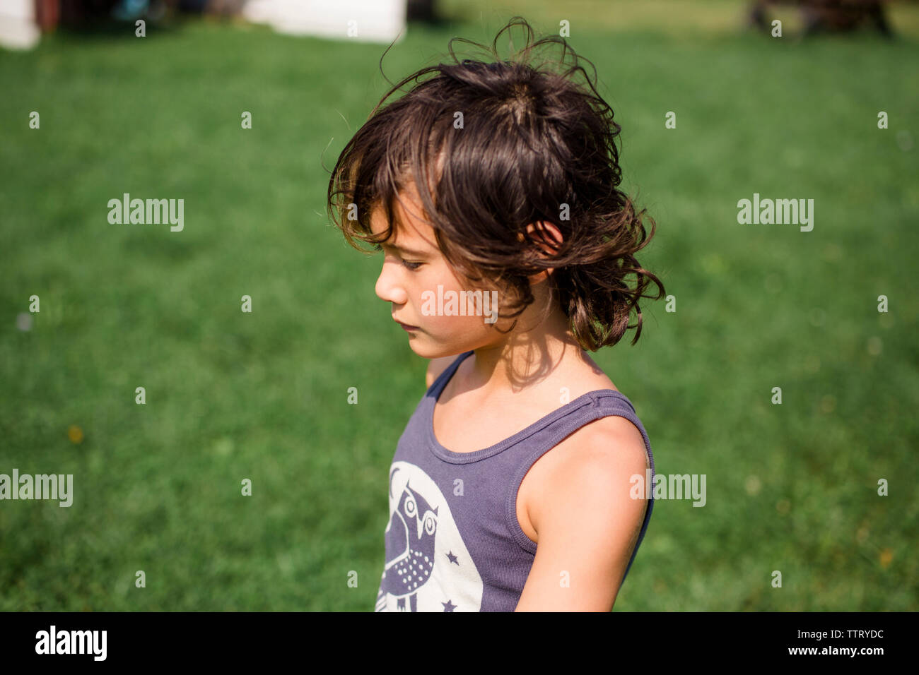 High angle view of thoughtful boy looking away while standing on grassy field in yard during sunny day Stock Photo