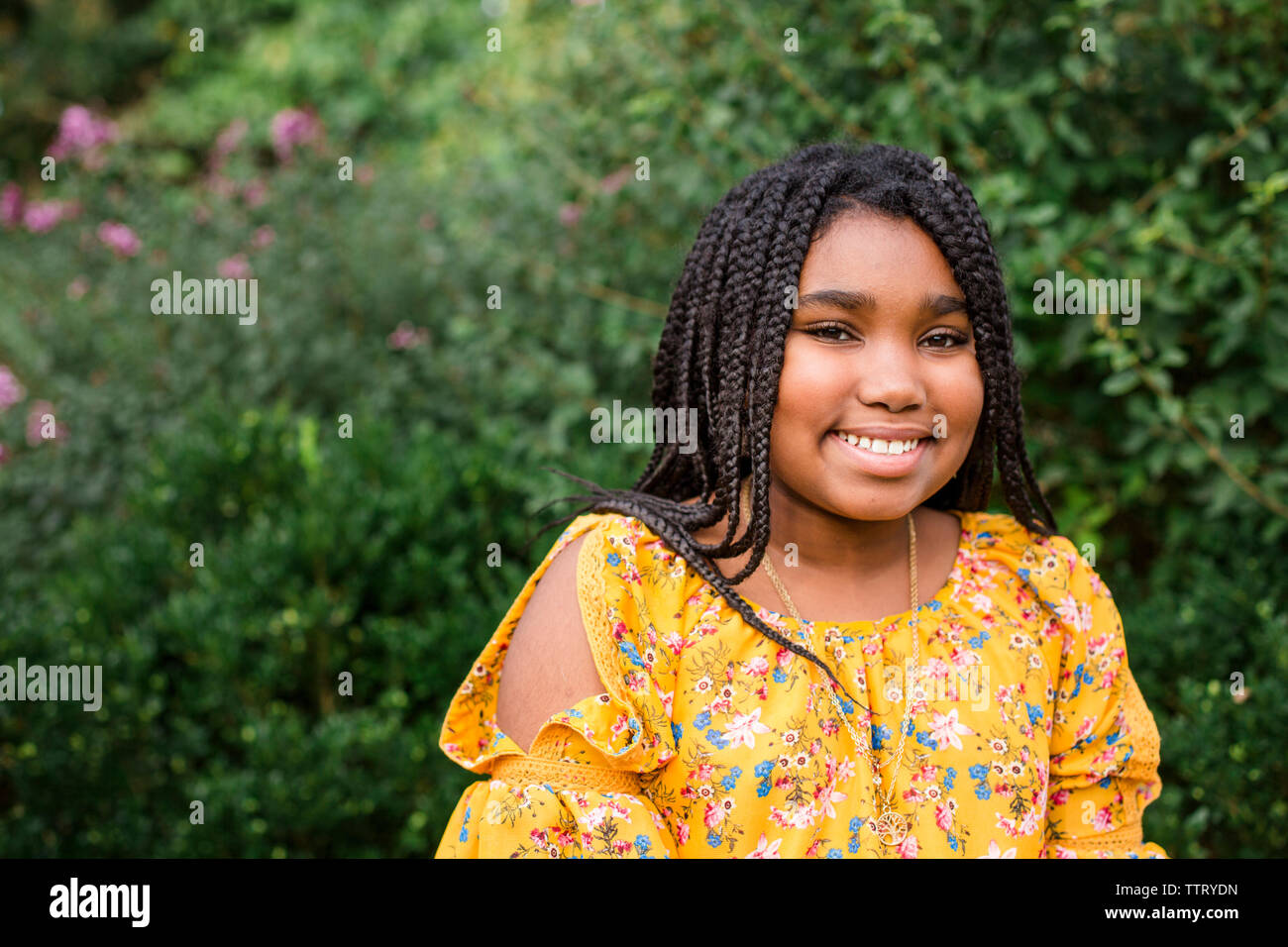 Portrait of smiling girl with braided hair sitting against plants in park Stock Photo