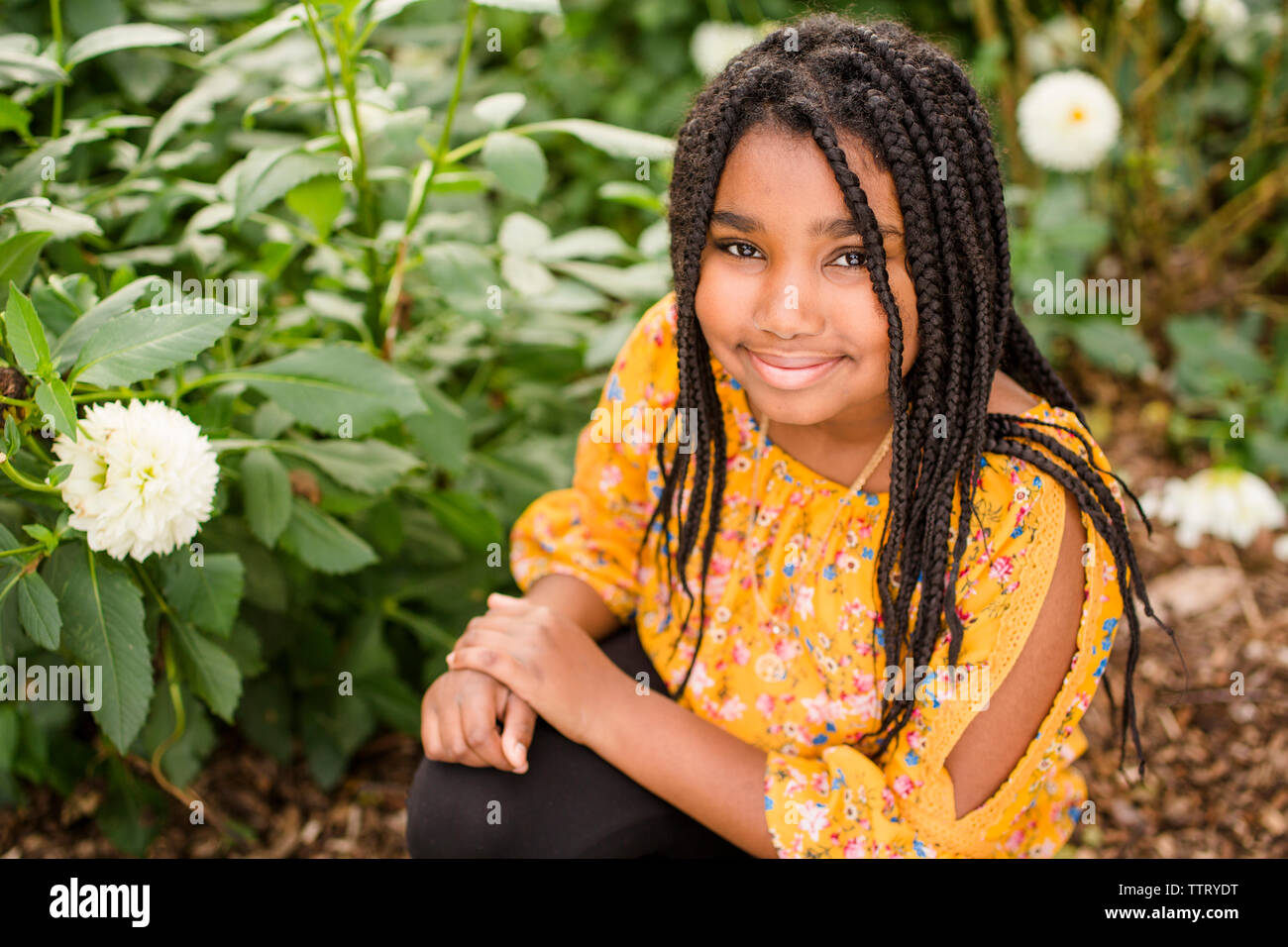 High angle portrait of smiling girl with braided hair crouching by plants in park Stock Photo
