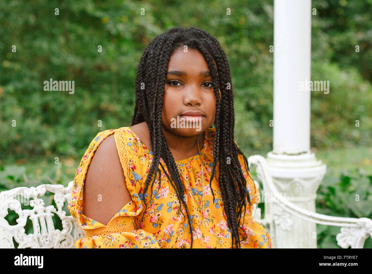 Portrait of girl with braided hair sitting on seat against plants in park Stock Photo
