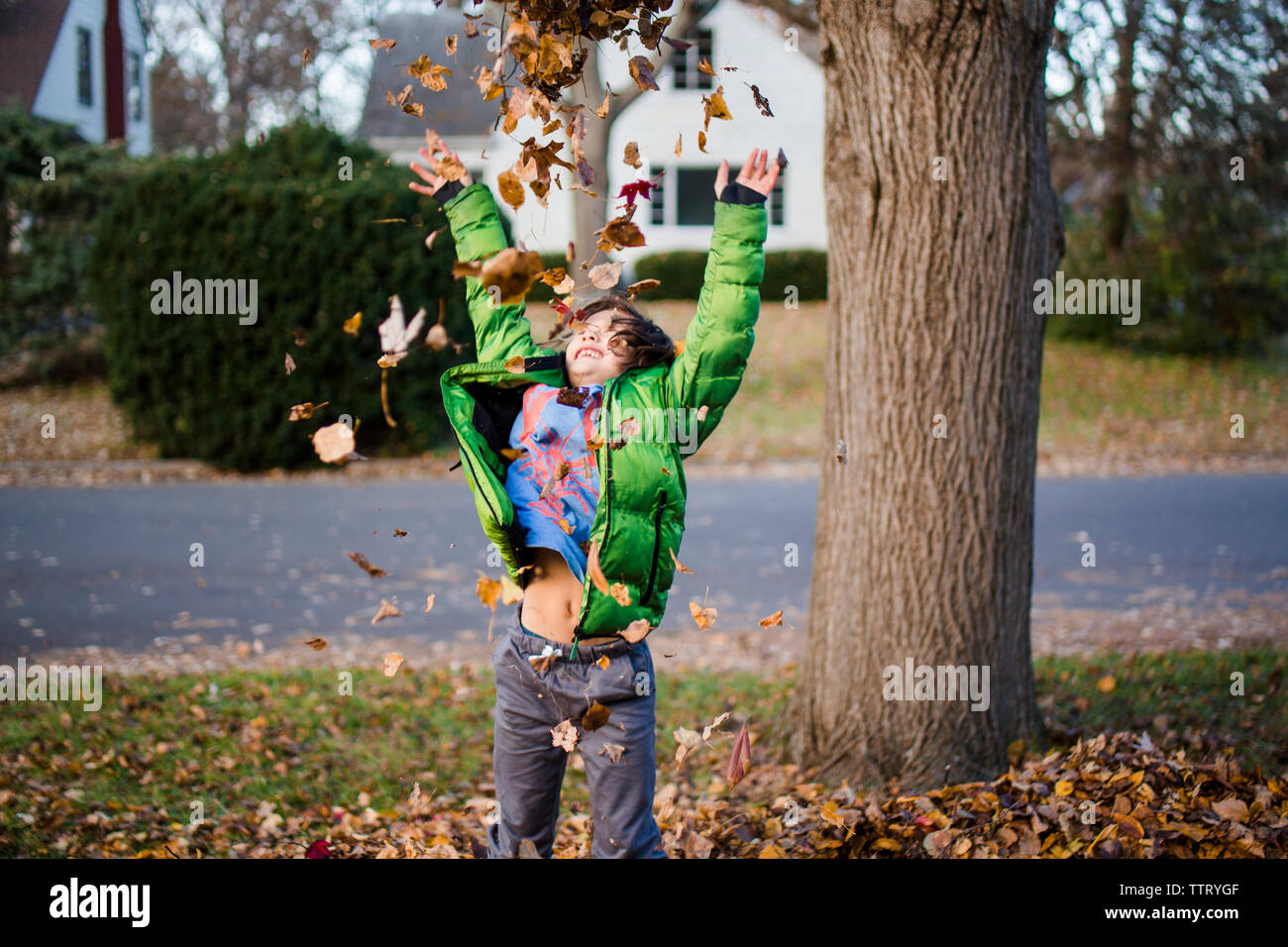 a happy, smiling boy with his arms up, throws leaves into the air Stock Photo