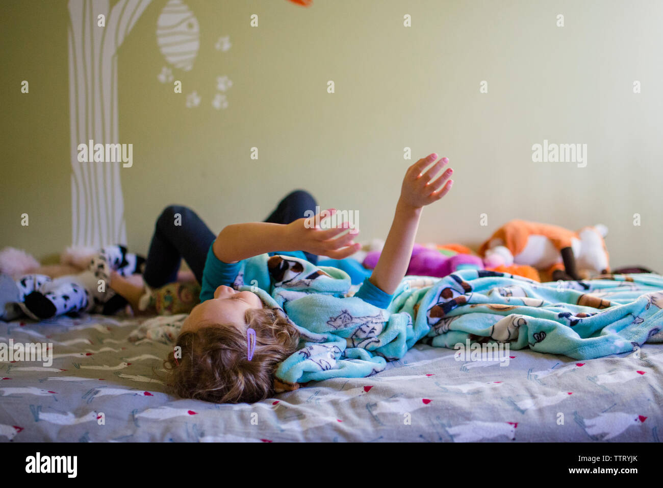A little girl daydreams in her bedroom wrapped in a blanket Stock Photo