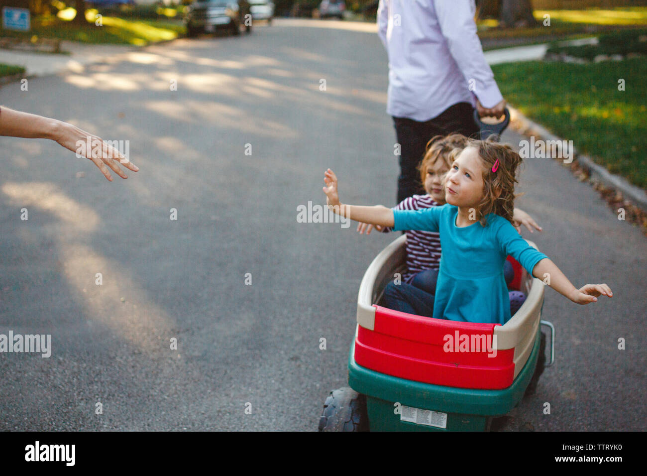 Parents walk down the street pulling two little girls in a wagon Stock