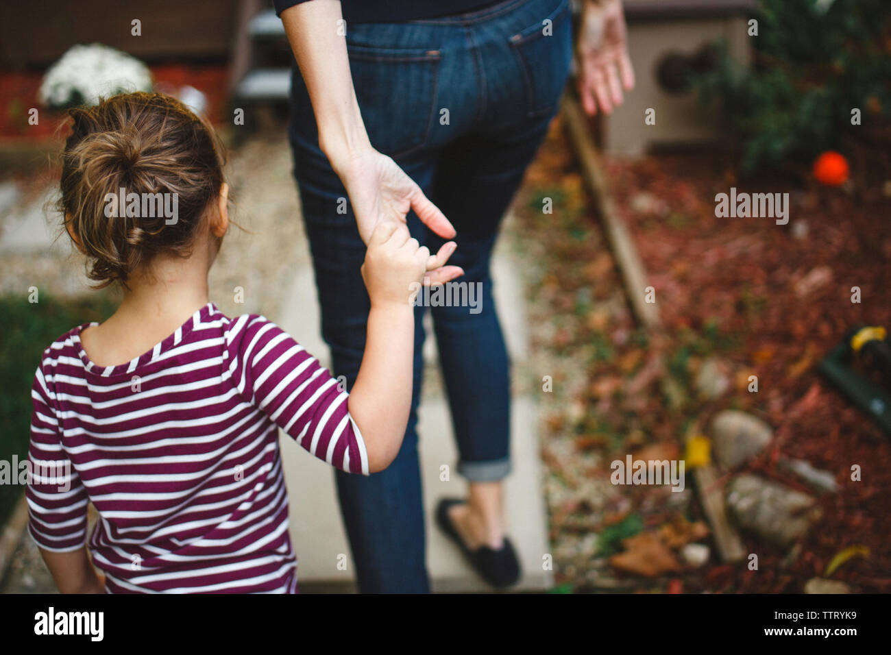 a toddler girl reaches up to hold her mothers hand as they walk Stock Photo