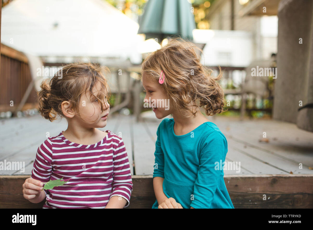 two little girls sit happily on a deck in conversation Stock Photo