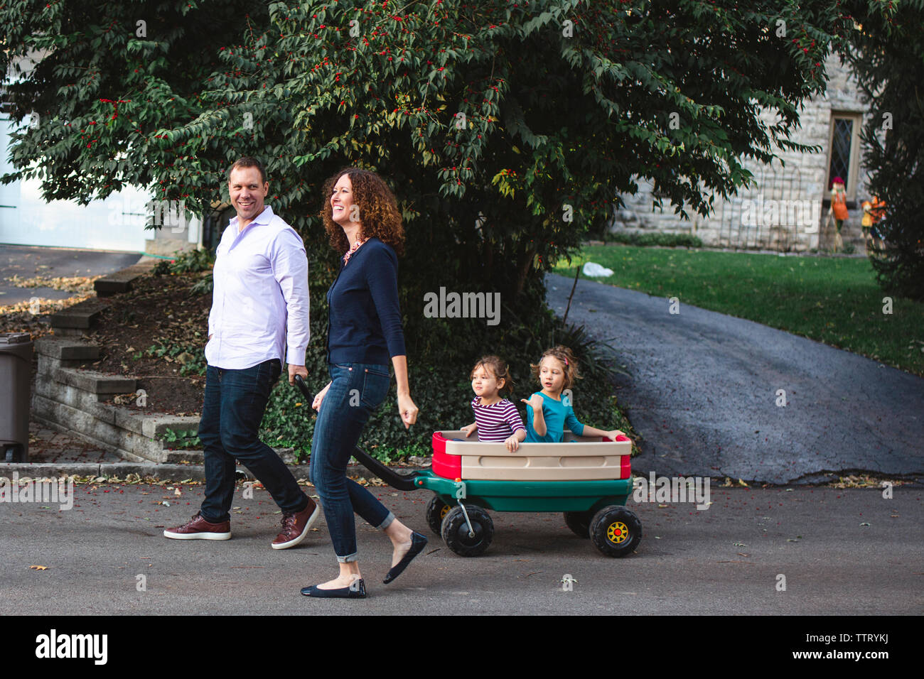 A happy family walks together down the street, children in a wagon Stock Photo