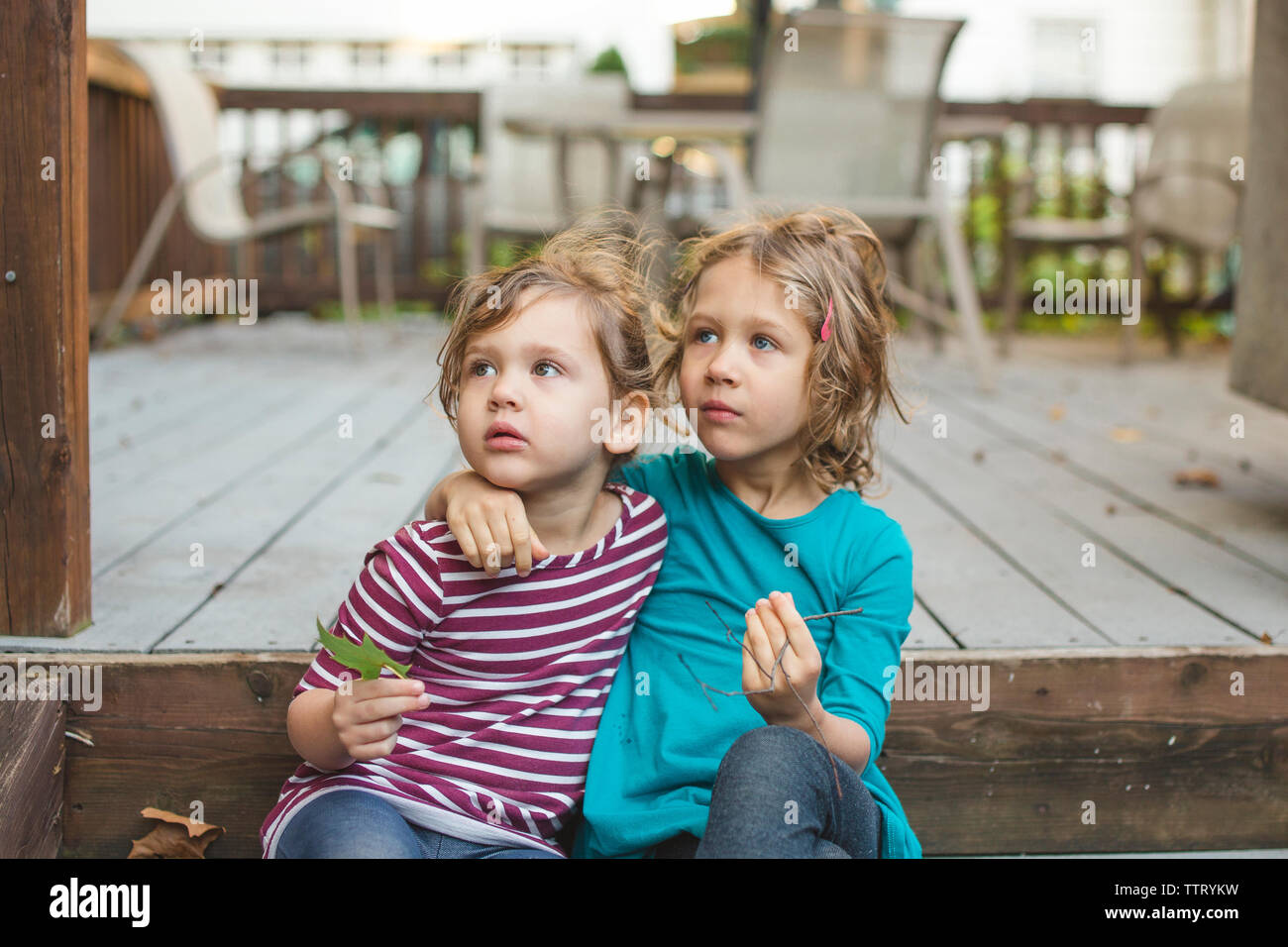 two little girls with their arms around each other sit outside Stock Photo