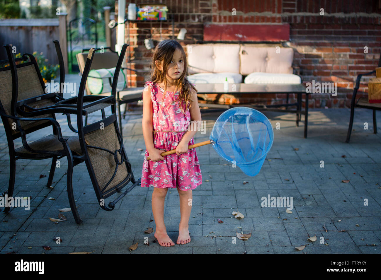 A small girl stands barefoot with a butterfly net in her hands. Stock Photo