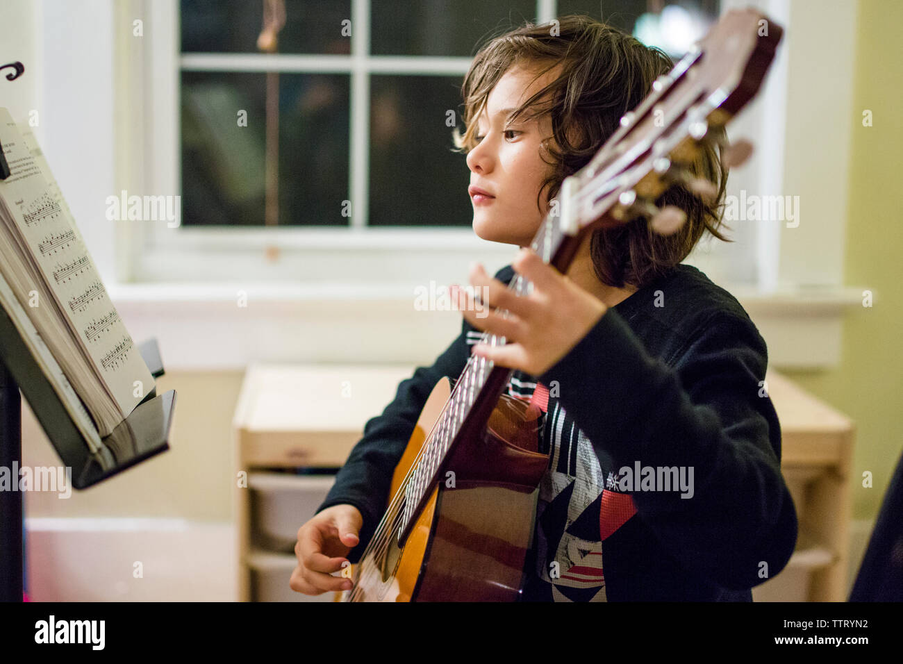 a boy studies sheet music as he practices guitar Stock Photo