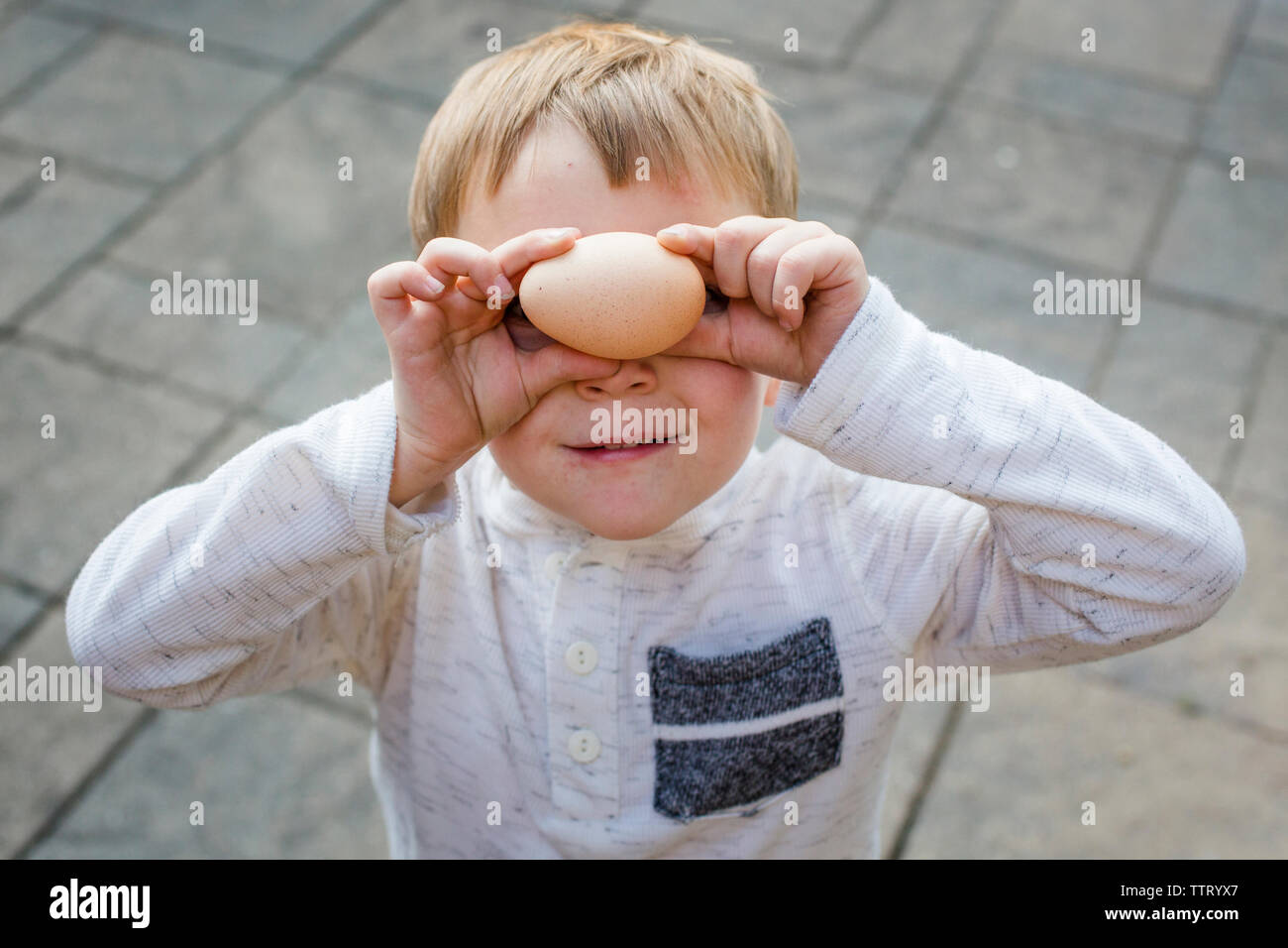 A small boy holds a chicken egg up to his eyes Stock Photo