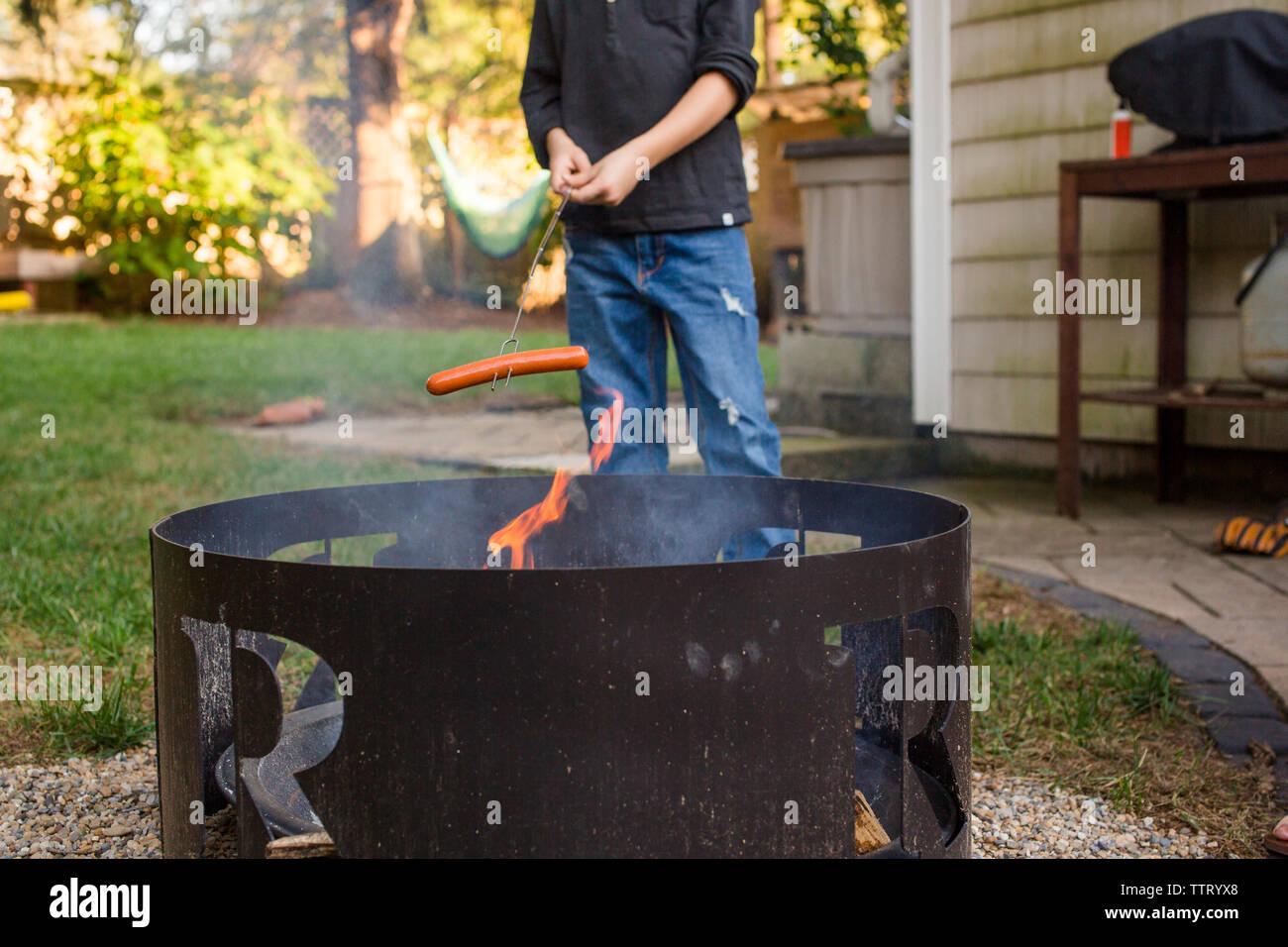 The Bottom Half Of A Boy Roasting Hot Dog Over Outdoor Fire Pit