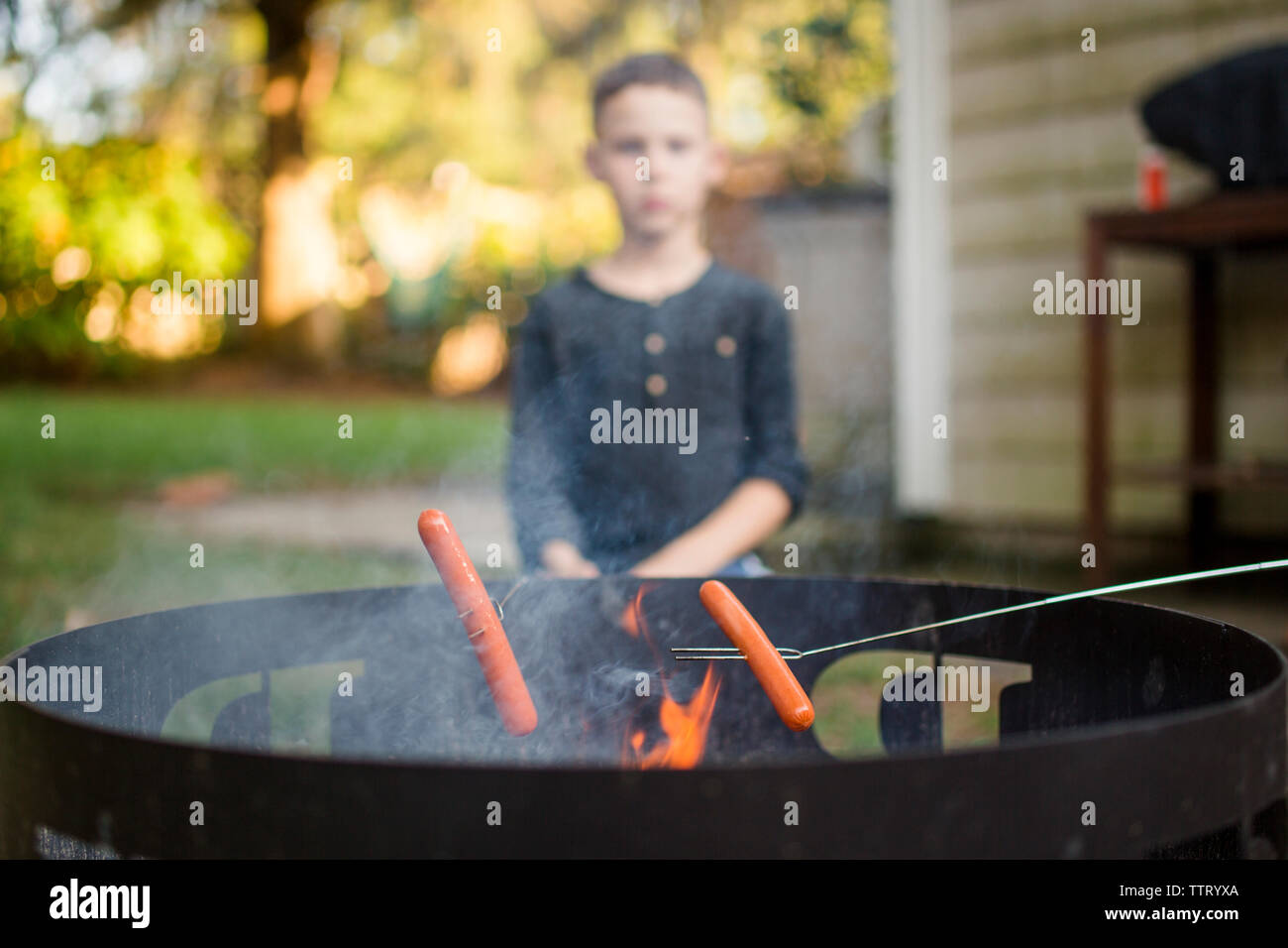 A boy roasting hot dogs with his family on an outdoor fire pit Stock Photo