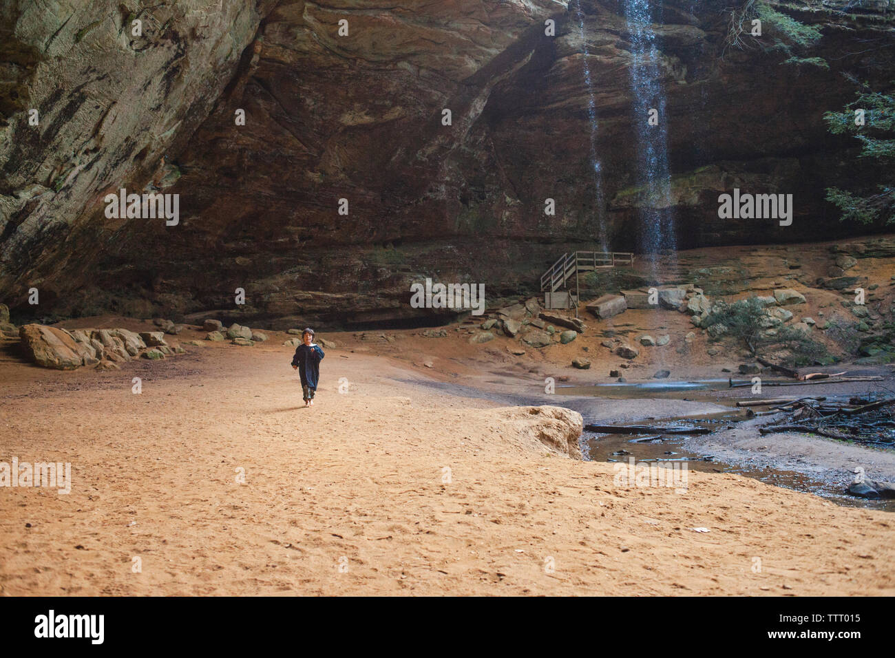 A small child in the distance standing in a gorge with waterfall Stock Photo