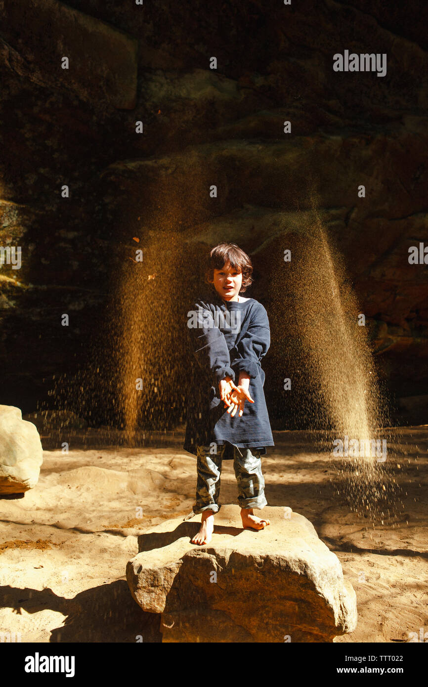 A small barefoot child throws golden sand into the air in sunlit gorge Stock Photo