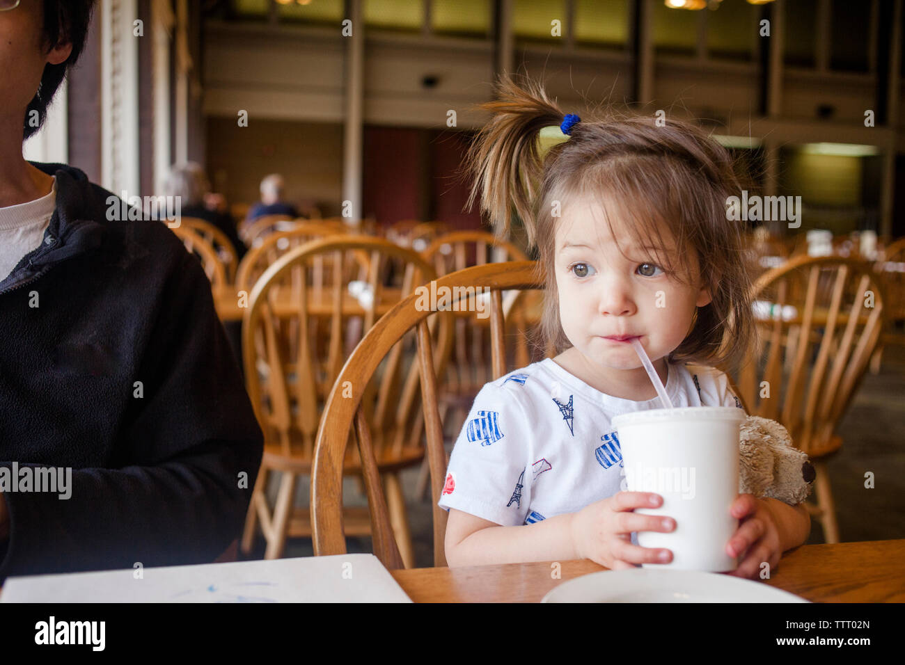 A small girl sits in a restaurant with her father sipping from a straw Stock Photo