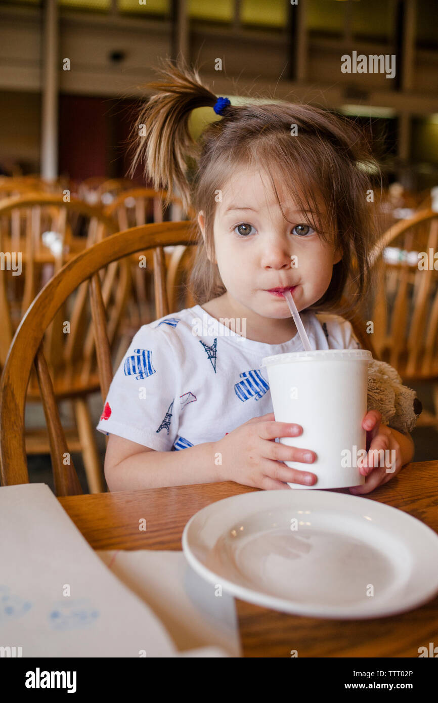 a cute little girl sips a drink out of a straw at a restaurant table Stock Photo