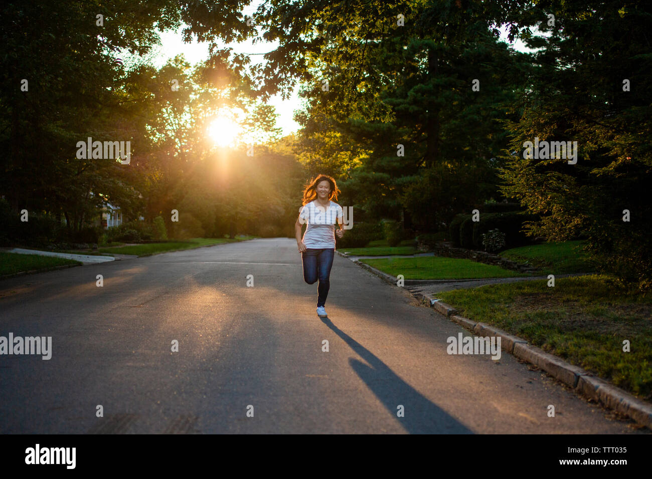 A teenage girl with flying hair runs alone on a street in golden light Stock Photo