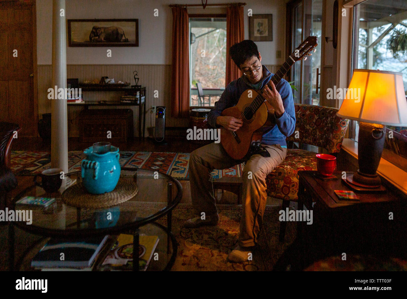 Portrait of a man playing guitar by himself in an eclectic home Stock Photo