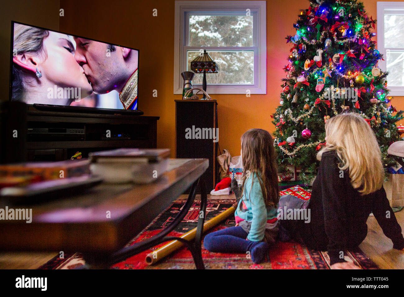 A mother and her little girl sit by a Christmas tree watching a movie Stock Photo