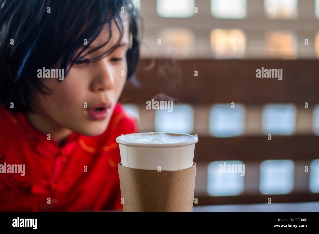 A small child sits at a cafe table blowing on a steamy cup of cocoa Stock Photo