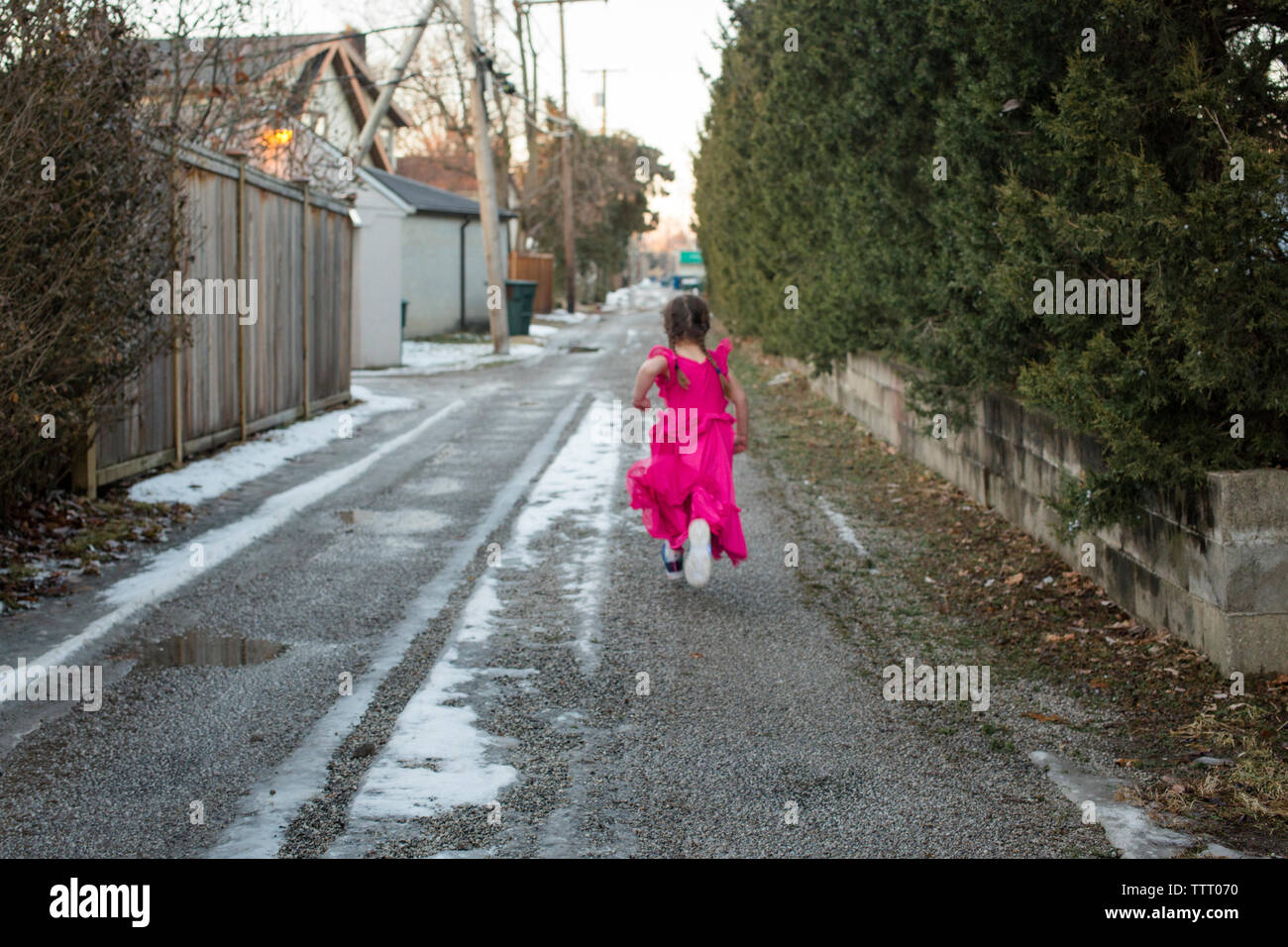 rear view of a little girl running in a long dress down a long alley Stock Photo