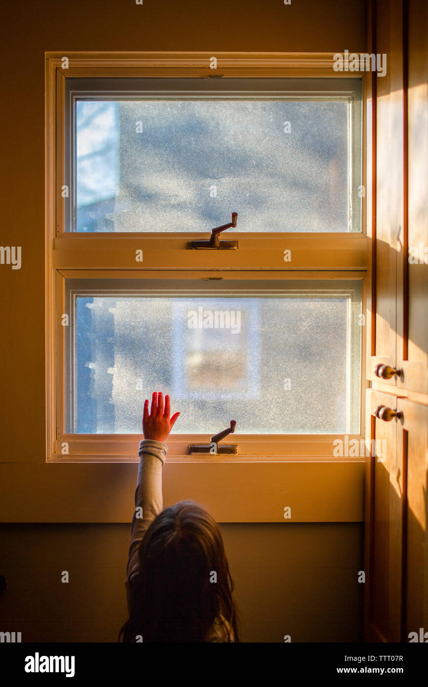 A small child reaches her hand up to sunlight streaming through window Stock Photo