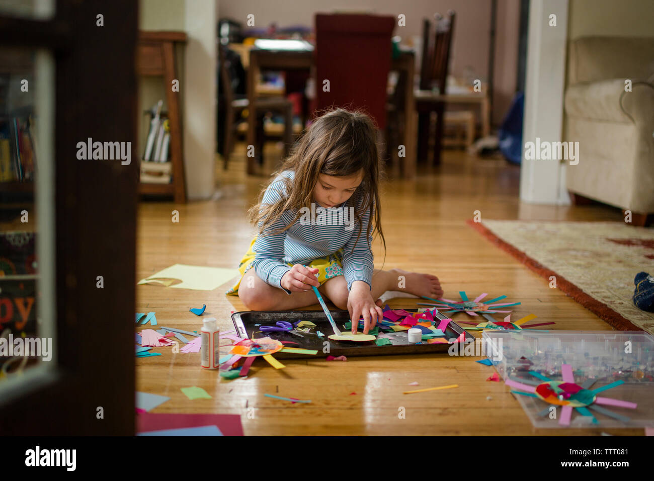 Looking through doorway at little girl sitting on floor crafting paper Stock Photo