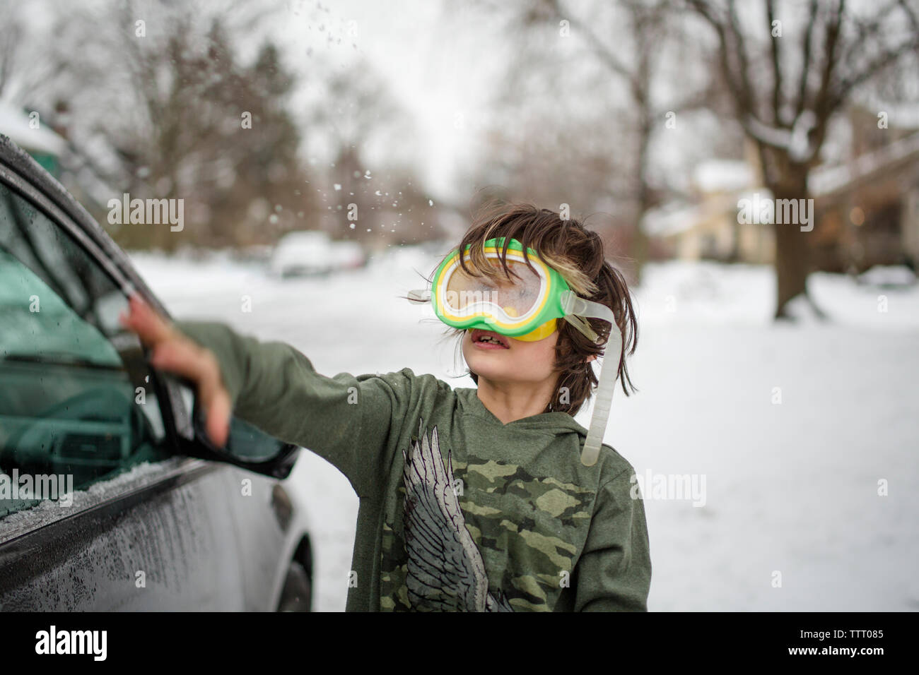 A small child wearing a snorkel mask plays in the snow on a winter day Stock Photo