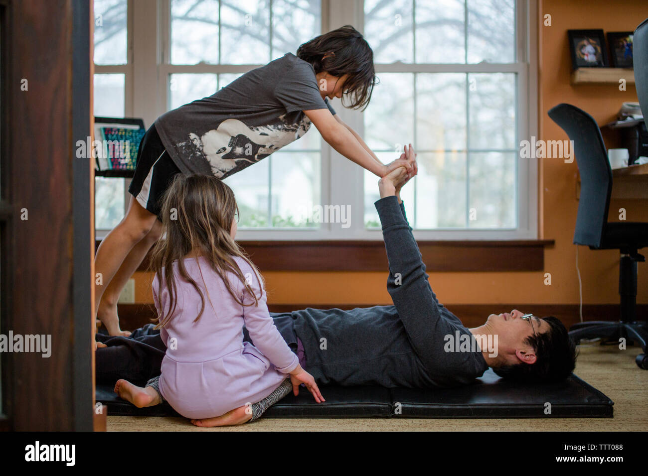 A father does exercise with his two small children inside a home Stock Photo