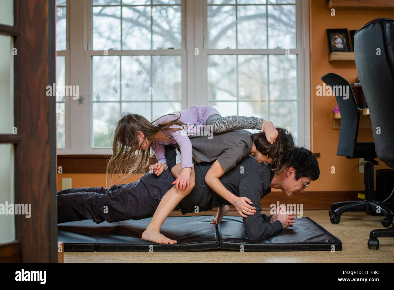 A father holds a plank position with two children piled on his back Stock Photo