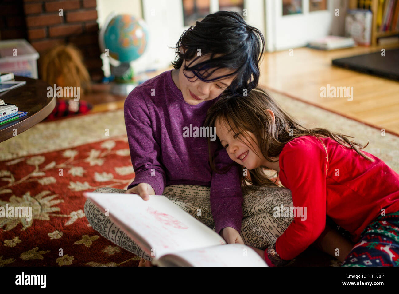 Two small children cuddle together on the living room floor reading Stock Photo